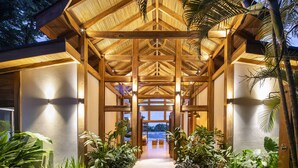A covered walkway with wooden beams and a thatched roof, leading to a seating area surrounded by tropical plants. - Villa Melody (Cóbano)