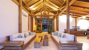 A spacious living area with wooden beams, a central seating arrangement, and a view through large windows. - Villa Melody (Cóbano)