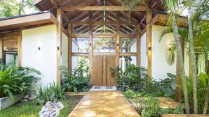 A wooden covered entrance with a herringbone floor leading to a door, surrounded by lush tropical plants. - Villa Melody (Cóbano)