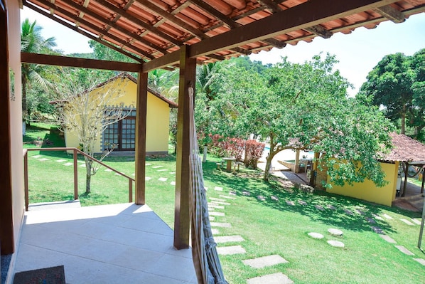 A covered outdoor area with a stone pathway leading to a yellow building, surrounded by lush greenery and trees.