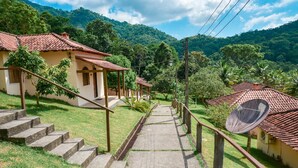 A pathway leading to a house with a red-tiled roof, surrounded by lush greenery and hills. - Pousada Vale dos Sonhos (Saquarema)