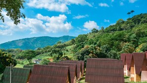 A row of simple, single-story cabins with sloped roofs, set against a backdrop of lush green hills and a clear blue sky. - Pousada Vale dos Sonhos (Saquarema)