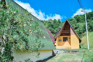 A small yellow building with a red roof, surrounded by greenery and a clear blue sky.