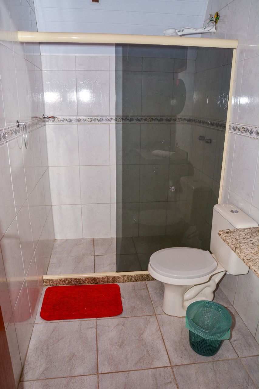 Casa de banho com cabine de duche, sanita e tapete de casa de banho vermelho.