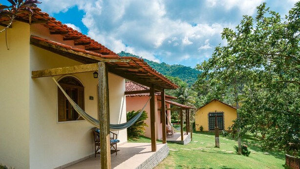 A two-story house with a red-tiled roof, a hammock, and a small patio area. - Pousada Vale dos Sonhos (Saquarema)