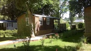 Eine kleine Holzhütte mit Veranda, umgeben von üppigem Grün und einem gepflegten Rasen.