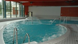 Ein beheiztes Hallenbad mit klarem Wasser, Metallgeländern und gefliestem Boden.