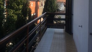 Ein Korridor mit einer gefliesten Wand, einem Metallgeländer und Blick auf ein Gebäude mit rotem Dach und Bäumen.