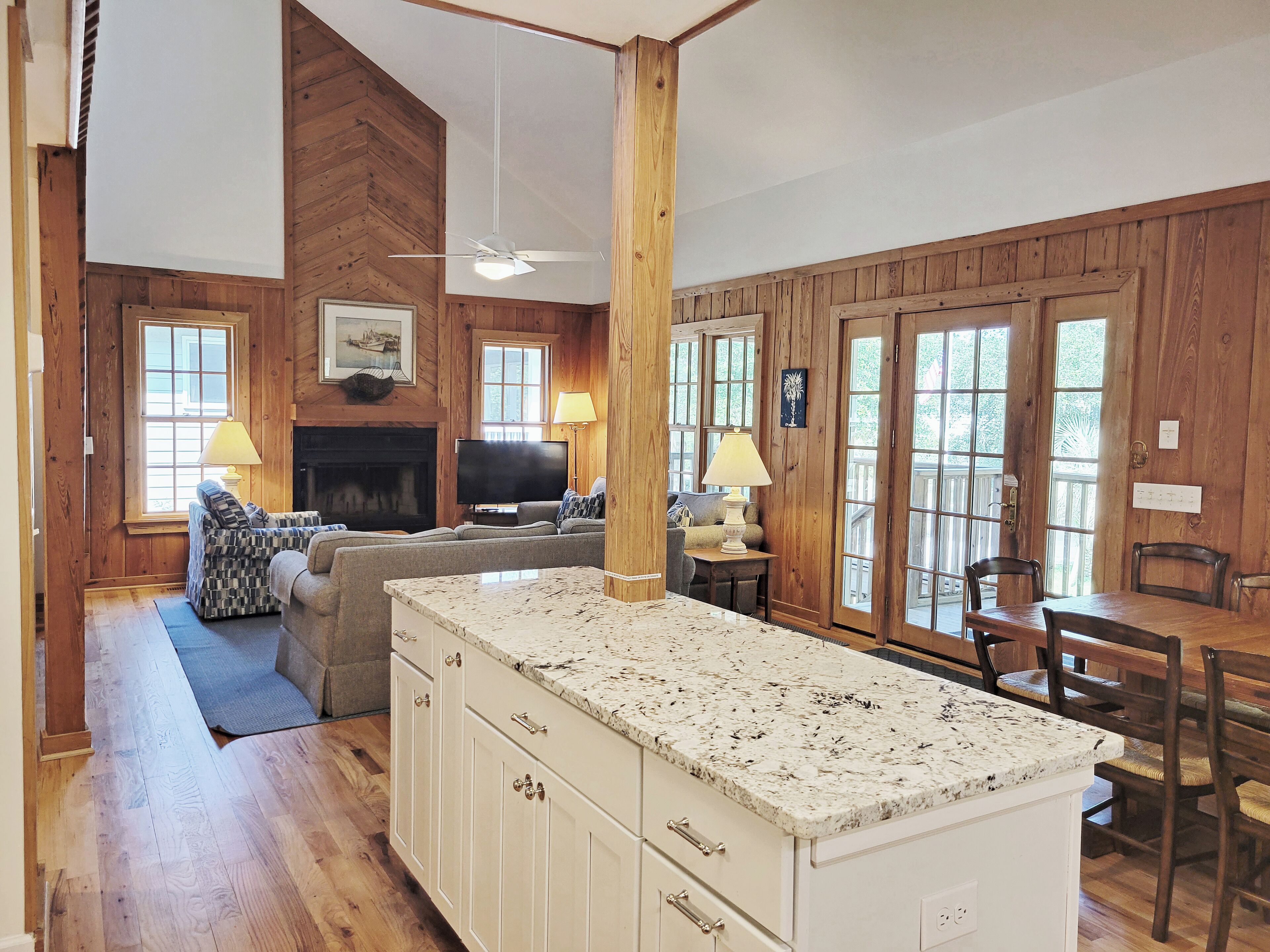 A spacious living area with a fireplace, wooden walls, a large window, and a dining area with a table and chairs.