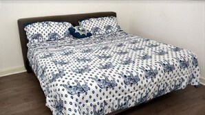 Ein Bett mit einem gemusterten Bettbezug und Kissen, ein Holz-Kopfbrett und eine schlichte Wand.