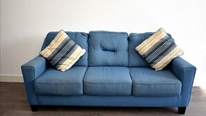 Ein blaues Sofa mit zwei gestreiften Kissen vor einer schlichten Wand.