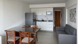Kompakti oleskelutila, jossa on ruokailualue, pieni keittiö ja harmaa sohva.