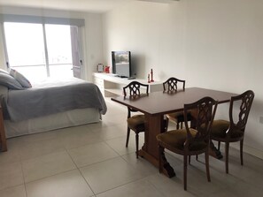 A bedroom with a bed, a TV, a desk, and a dining table with chairs. - Simpatico Loft Centrico (Salta)