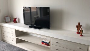 Valkoinen TV-taso, jossa on litteänäyttöinen televisio, pieni puinen koriste-esine ja muutama kirja.