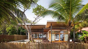 Une maison moderne avec une piscine, entourée d’une clôture en bois et de palmiers.
