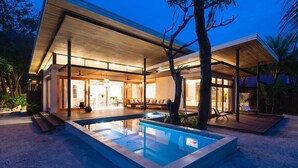 Une maison moderne dotée d’une piscine, de grandes fenêtres et d’un patio couvert.