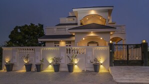 A modern two-story house with a gated entrance, multiple potted plants, and a well-lit facade. - Anagha Homestay Home Away From Home (Udaipur)