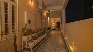 A corridor with potted plants on shelves, a patterned floor, and a staircase leading to another level. - Anagha Homestay Home Away From Home (Udaipur)