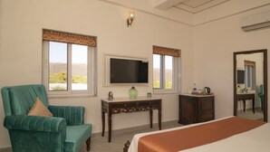 A hotel room with a large bed, a green armchair, a small table with a television, and a dresser. - Anagha Homestay Home Away From Home (Udaipur)
