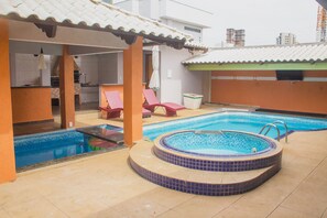 A swimming pool area with a hot tub, lounge chairs, and a covered seating area. - Palmas Hostel (Palmas)