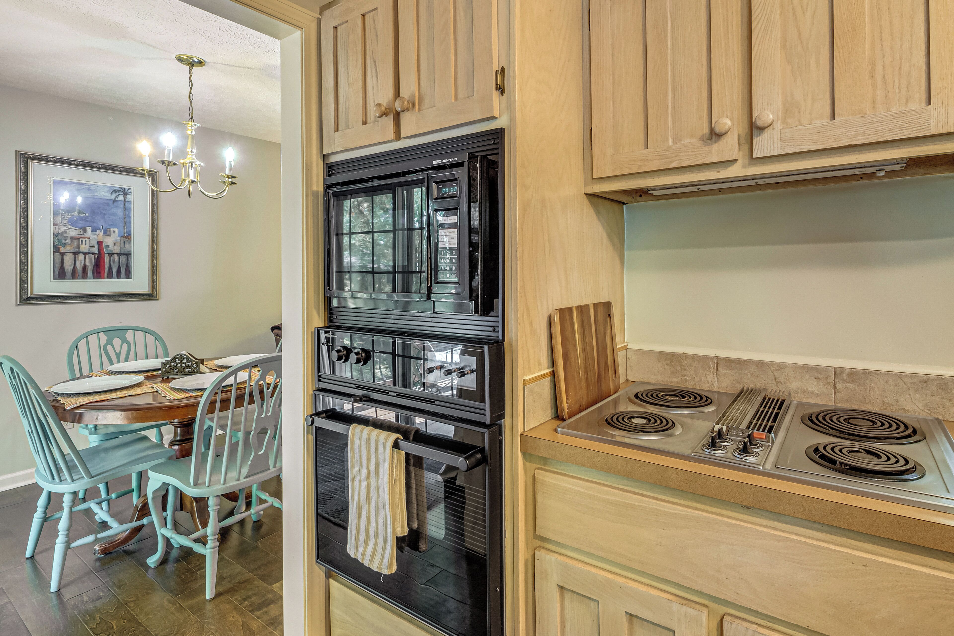 A kitchen with a black oven, a stove, wooden cabinets, and a dining area with teal chairs and a table.