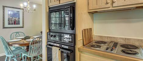 A kitchen with a black oven, a stove, wooden cabinets, and a dining area with teal chairs and a table.