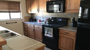A kitchen with wooden cabinets, a black stove, a microwave, and a refrigerator. - Your next, beautiful getaway! (Hunt)