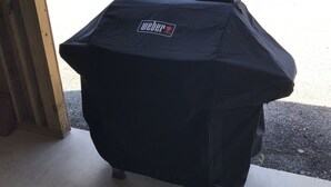A covered grill with a Weber logo, placed outdoors on a concrete surface. - Your next, beautiful getaway! (Hunt)