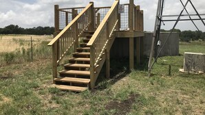 A wooden staircase leading to a platform with a metal guardrail and a sign that reads "NO LIFEGUARD ON DUTY." - Your next, beautiful getaway! (Hunt)