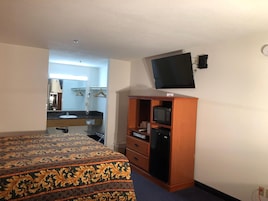 A hotel room with a bed, a wooden wardrobe, a television mounted on the wall, and a bathroom visible through an open door.