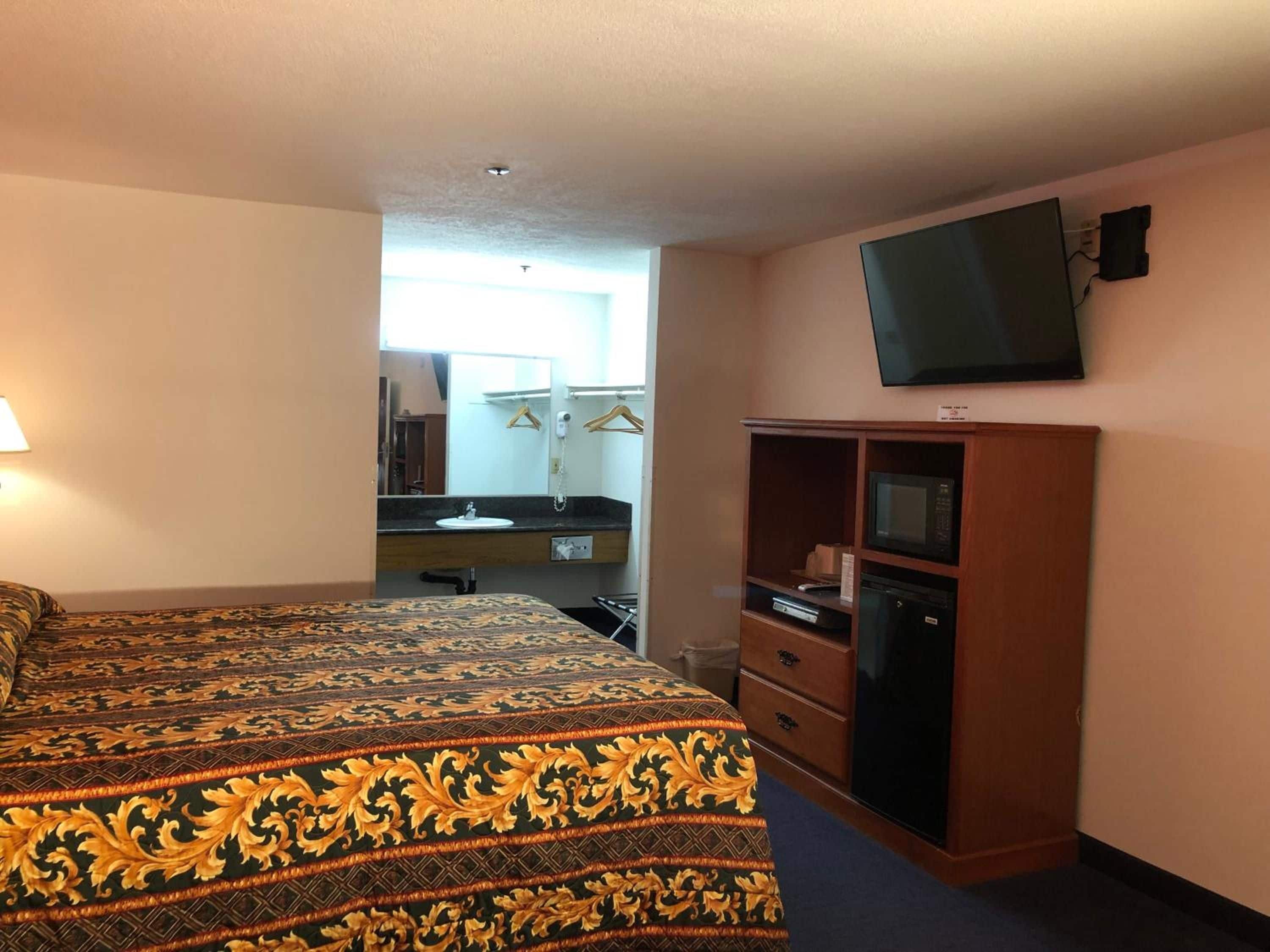 A hotel room with a bed, a television mounted on the wall, a wooden cabinet, and a bathroom visible through an open door.
