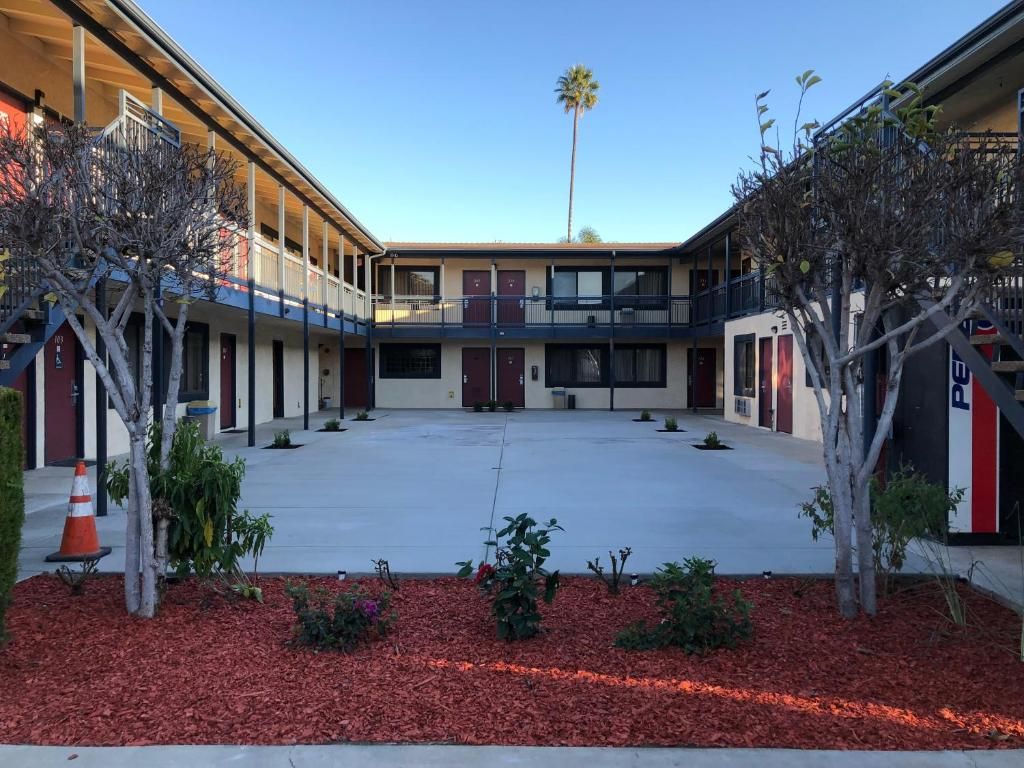 A courtyard with a building featuring multiple balconies, a palm tree, and a parking area.