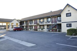 Un motel doté d’un parking central, de plusieurs chambres avec balcon et d’un escalier menant à l’étage supérieur.