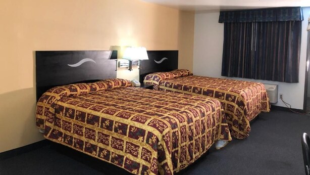 A hotel room with two beds, a nightstand, a lamp, a television, and a window with curtains. - Luxury Inn (Norwalk)
