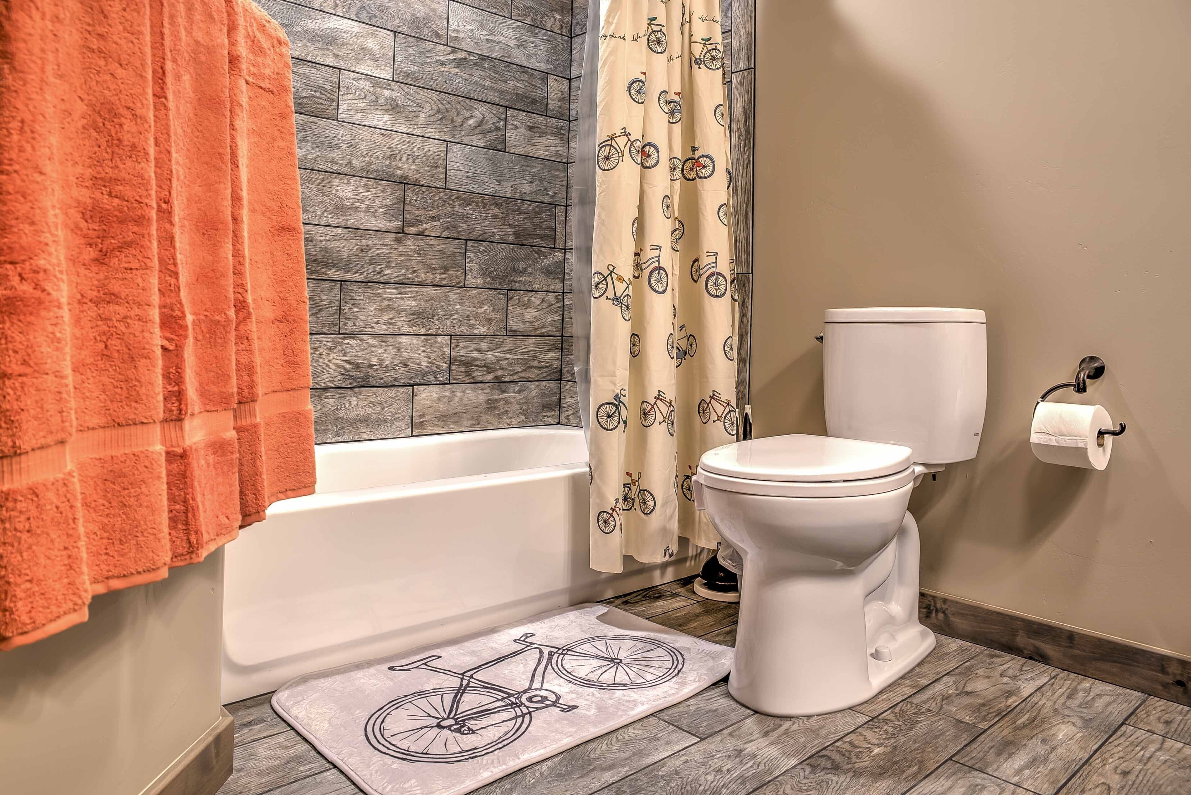 A bathroom with a wooden floor, a white toilet, a bathtub, and a bicycle-themed rug.