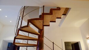 Una escalera de caracol con escalones de madera y barandillas de metal en una habitación con paredes blancas y techo de madera.