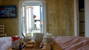 Desayuno con pan, mantequilla y utensilios sobre una tabla de madera, con vista al exterior a través de una puerta abierta.