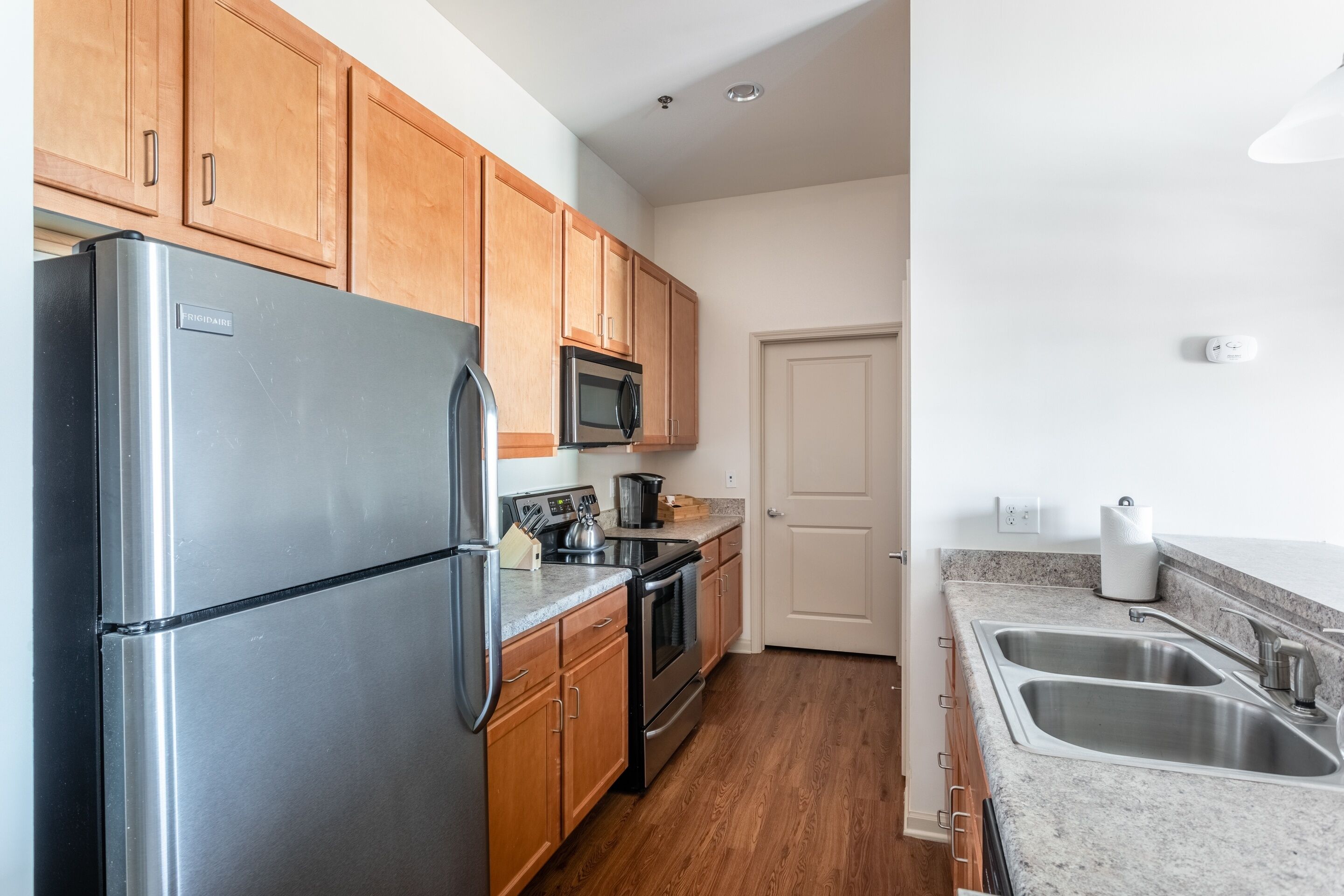 A modern kitchen with stainless steel appliances, wooden cabinets, a double sink, and a microwave.