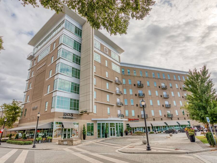 A multi-story hotel with a modern design, featuring a central entrance, outdoor seating area, and a parking lot.