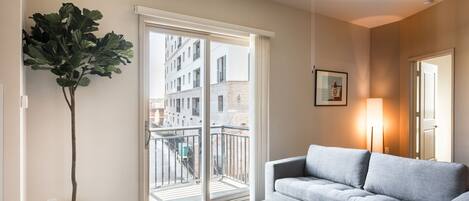 A modern living room with a grey sofa, a coffee table, a large window with a view of buildings, and a ceiling fan.