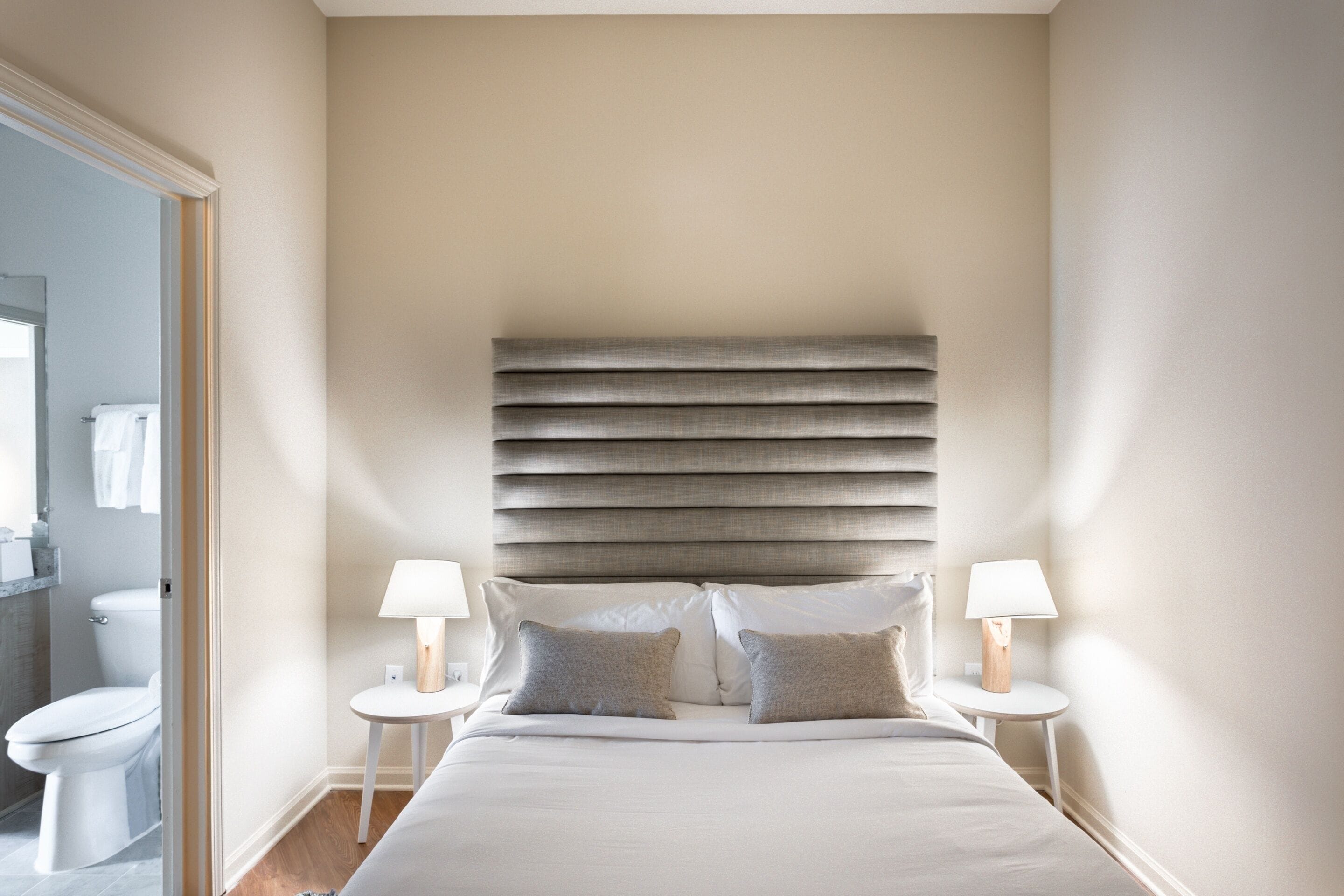 A bedroom with a large bed, two bedside tables with lamps, a headboard, and a view of a bathroom.