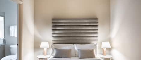 A bedroom with a large bed, two bedside tables with lamps, a headboard, and a view of a bathroom.