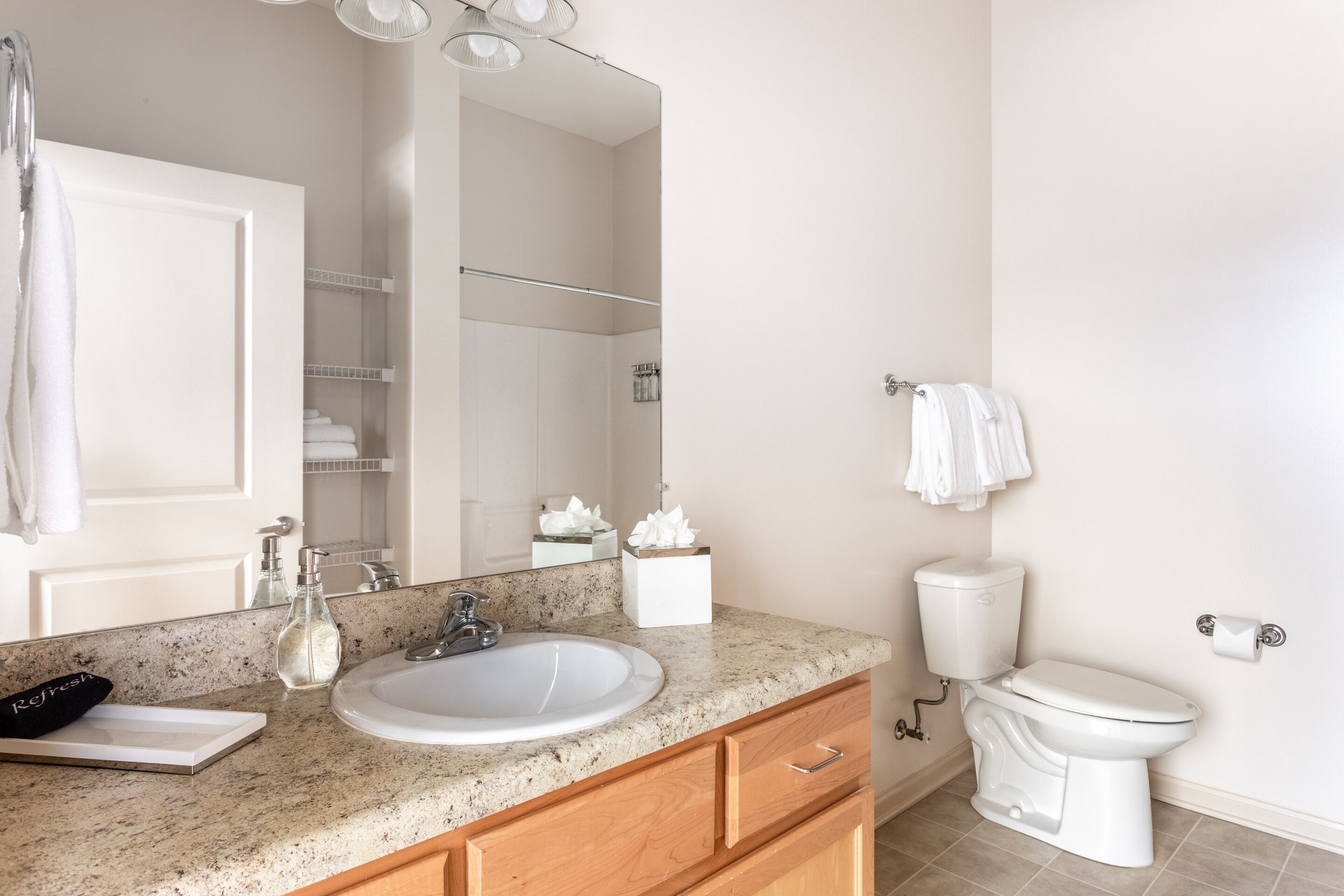 A bathroom with a white sink, wooden cabinets, a mirror, a toilet, and a towel rack.