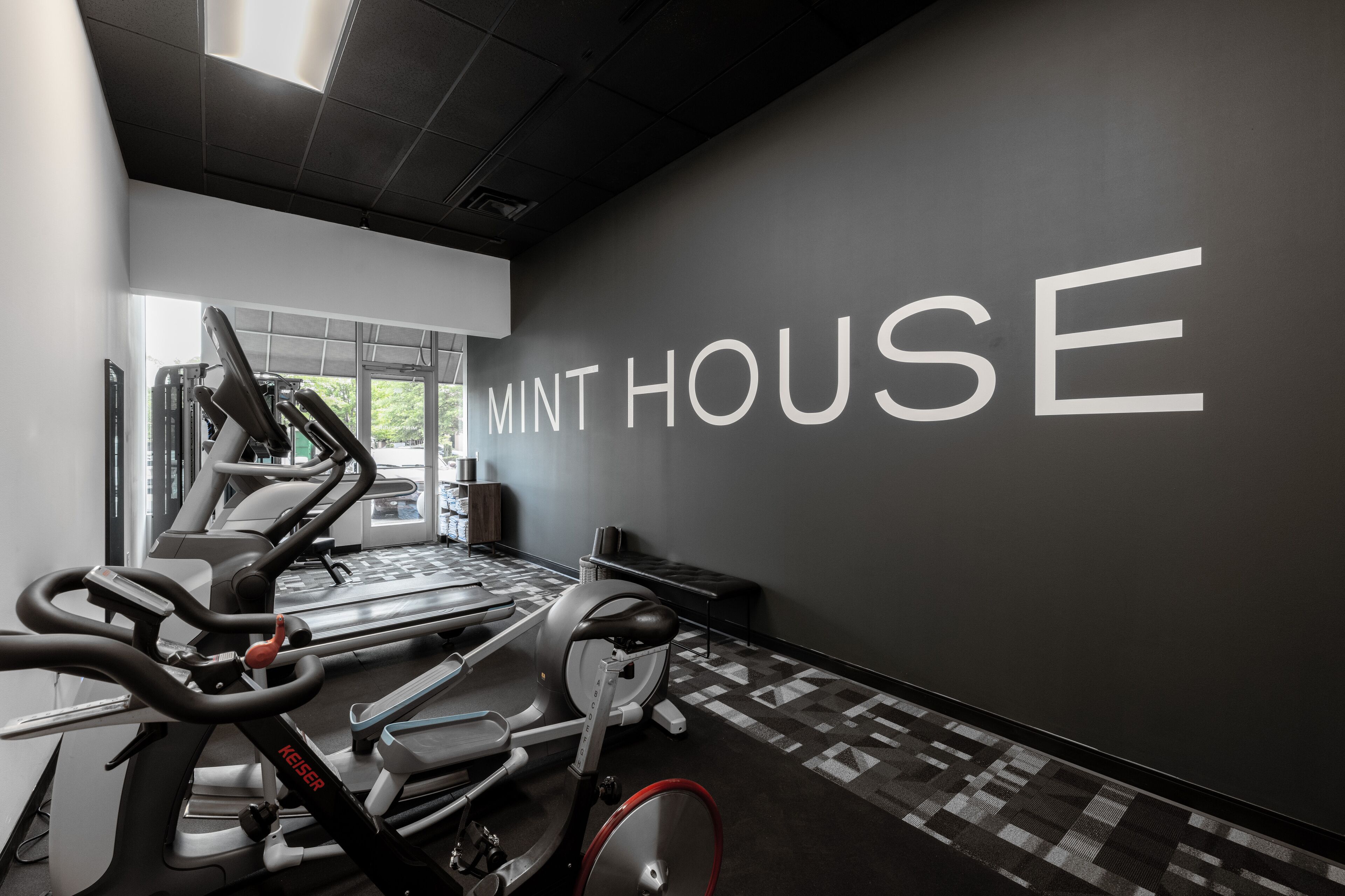 Une salle de sport équipée de tapis de course, de vélos elliptiques et d’un mur sur lequel est inscrit le texte « MINT HOUSE ».