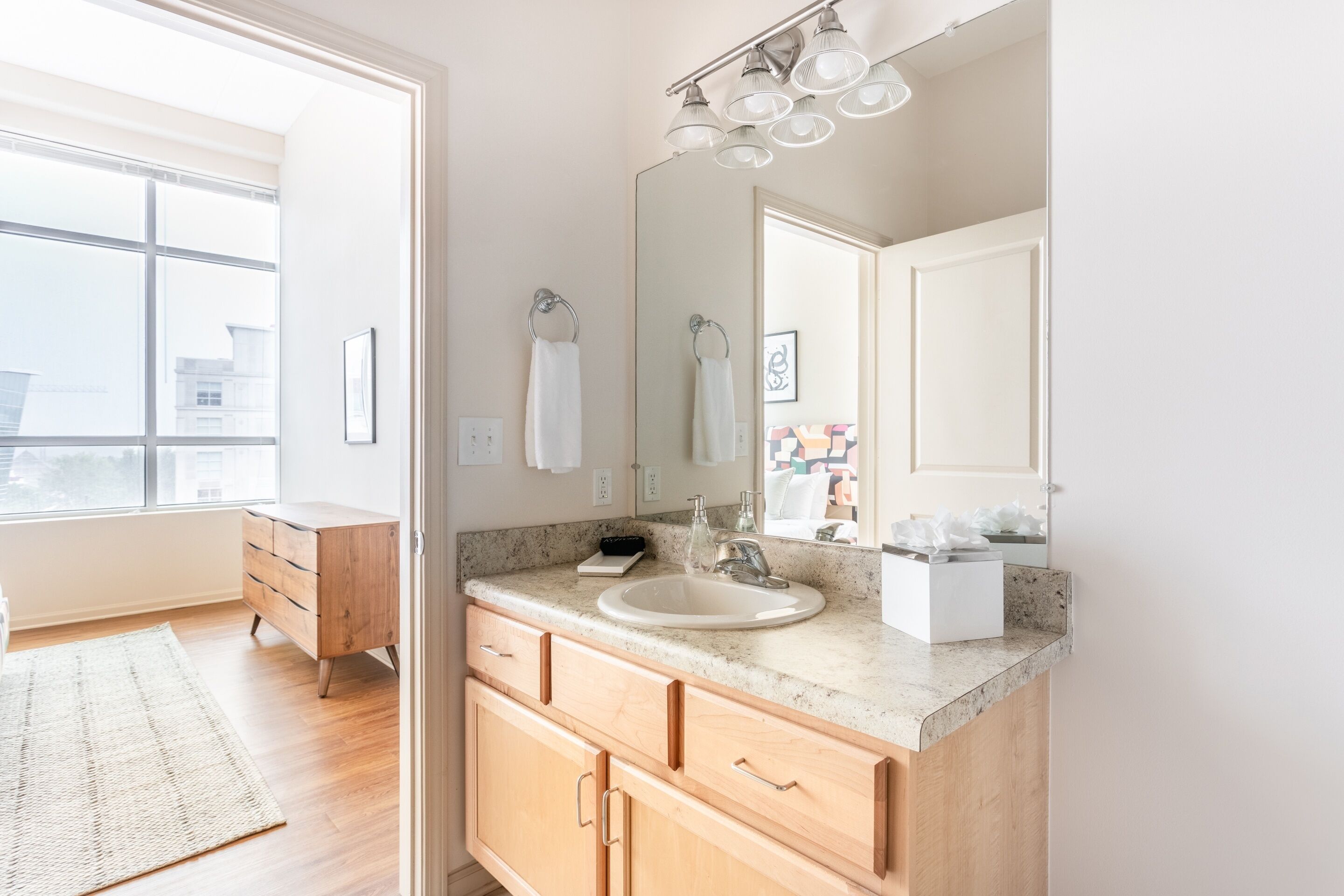 A modern bathroom with a large window, a sink, a mirror, and wooden cabinets.