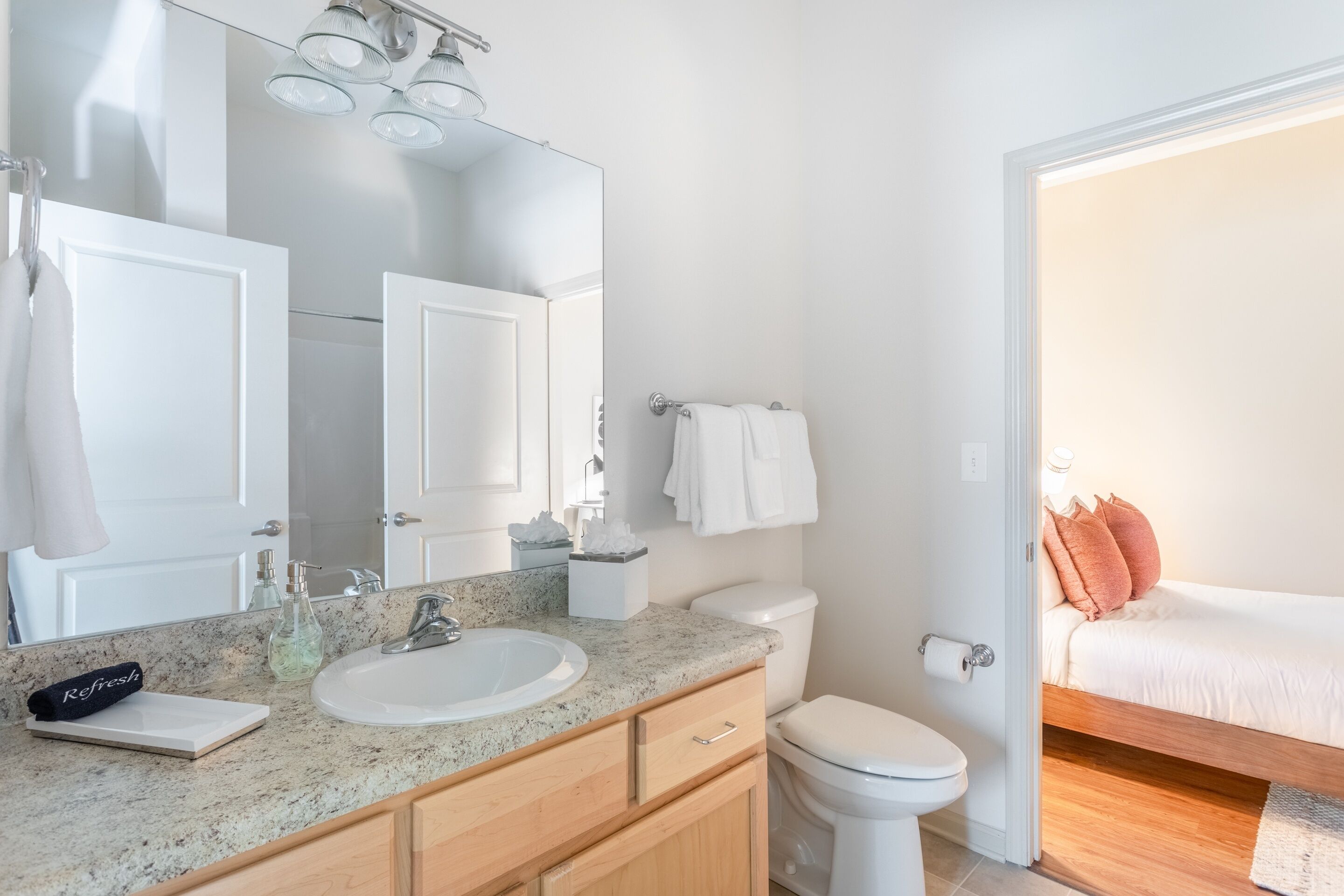 A modern bathroom with a granite countertop, white fixtures, and a large mirror.
