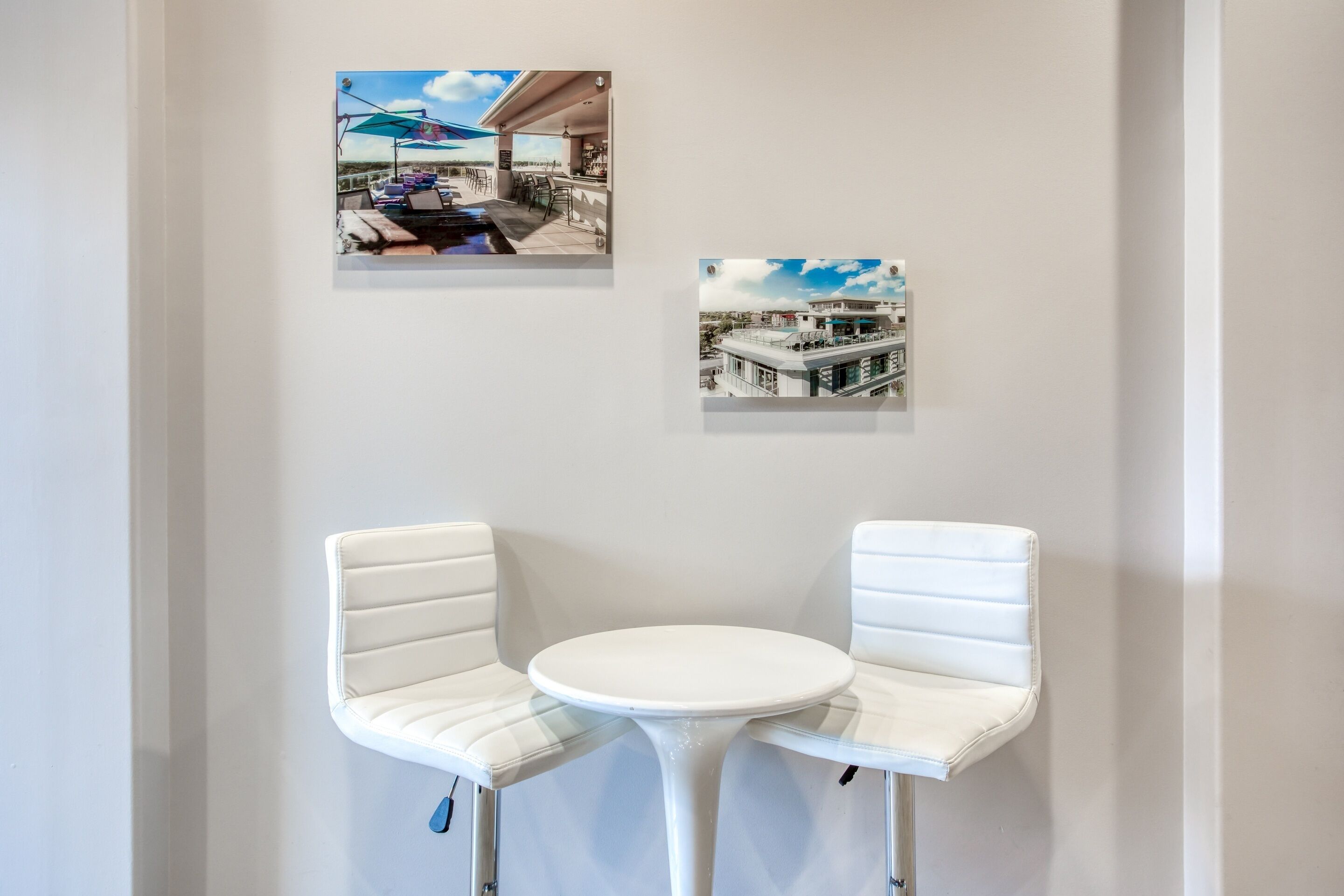 A corner with two white cushioned chairs and a small round table, with two framed photographs on the wall above.