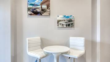 A corner with two white cushioned chairs and a small round table, with two framed photographs on the wall above.