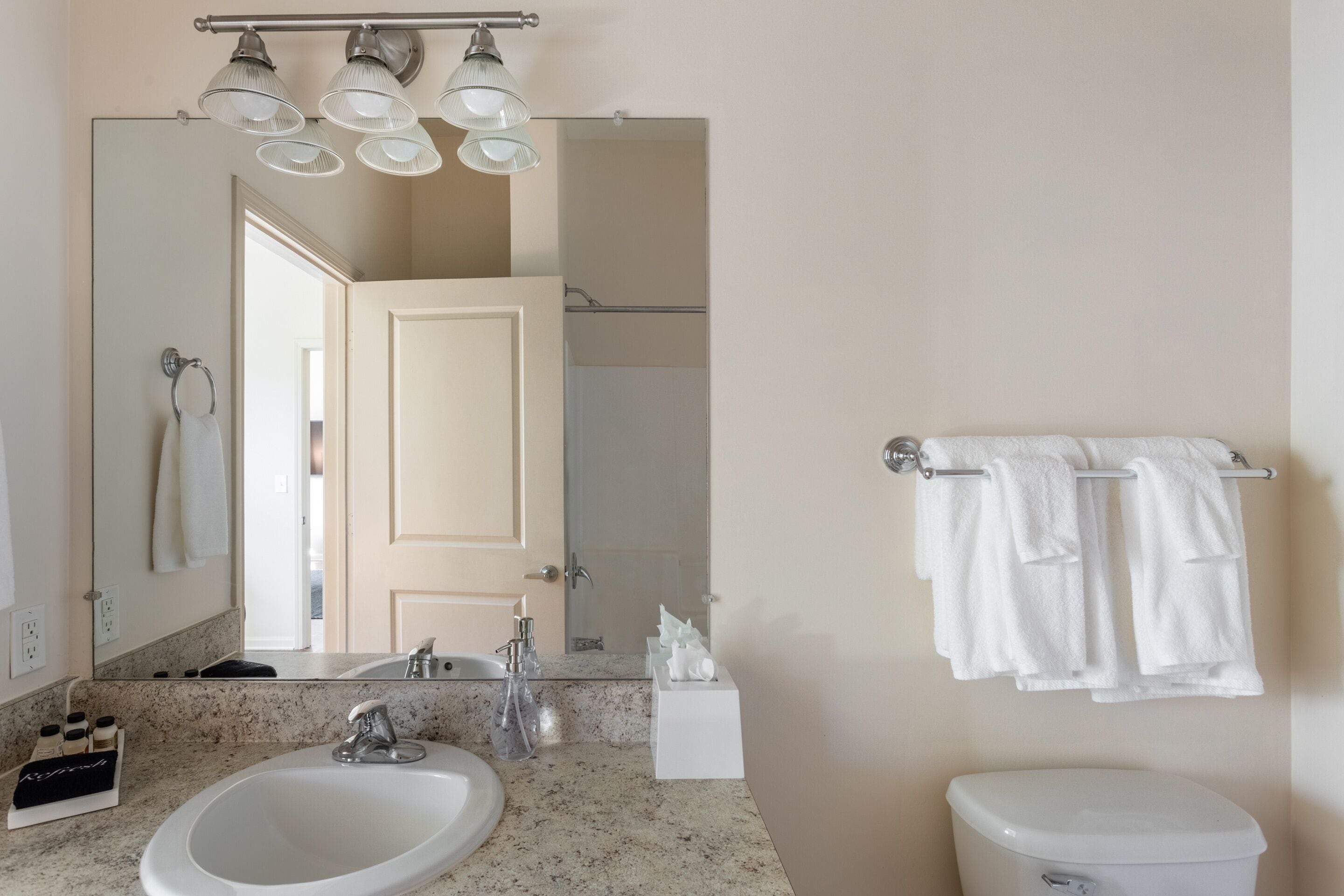 Un baño con lavamanos, espejo, toallero y retrete.