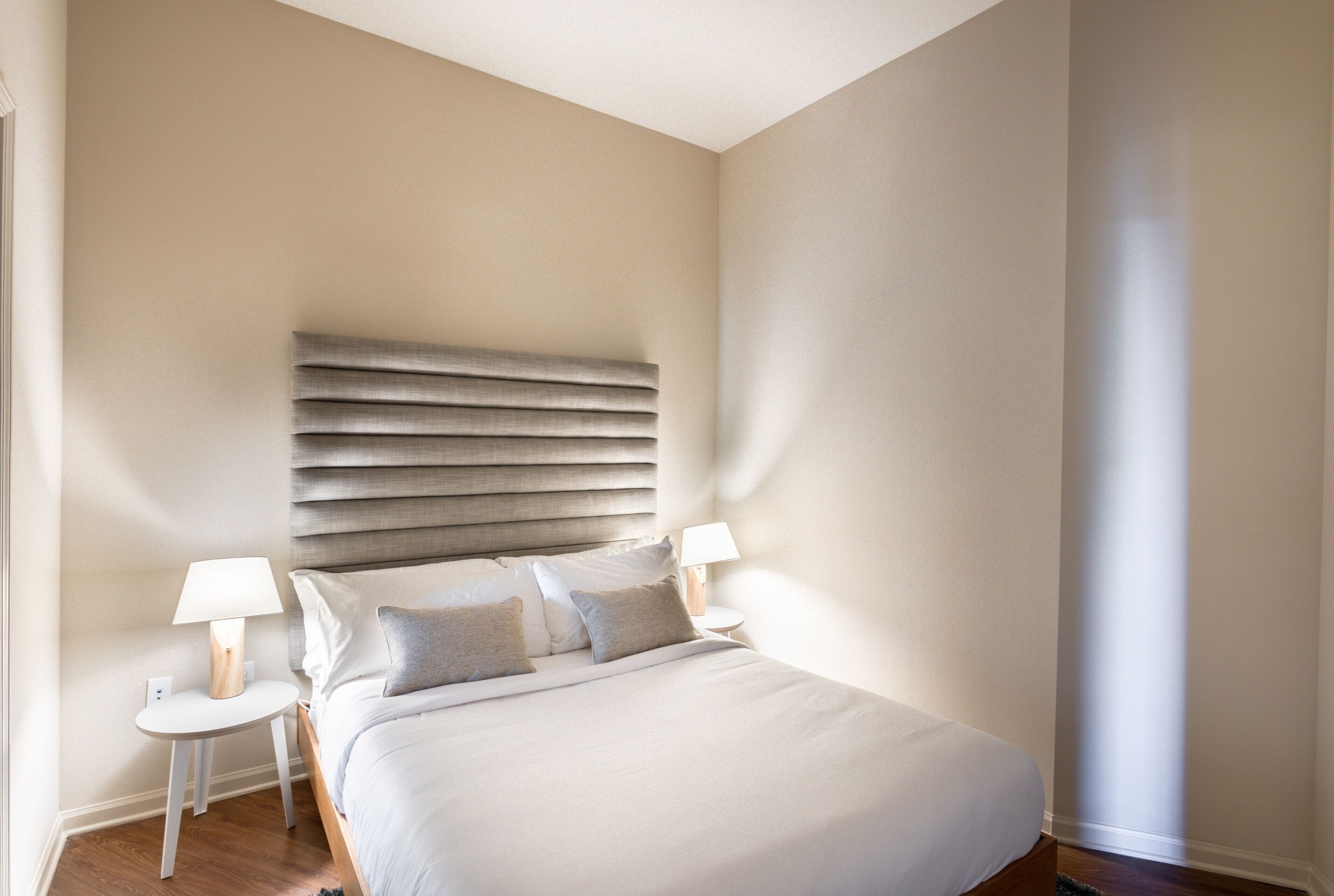 A neatly made bed with a headboard, two bedside tables with lamps, and a window on the right.